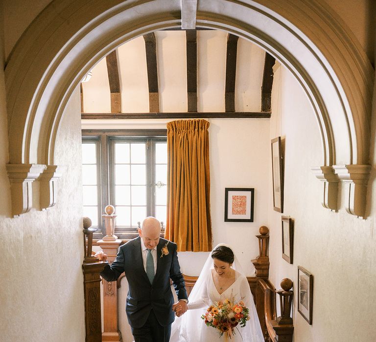 Father of the bride walks down the stairs hand in hand with the bride on the way to the church 