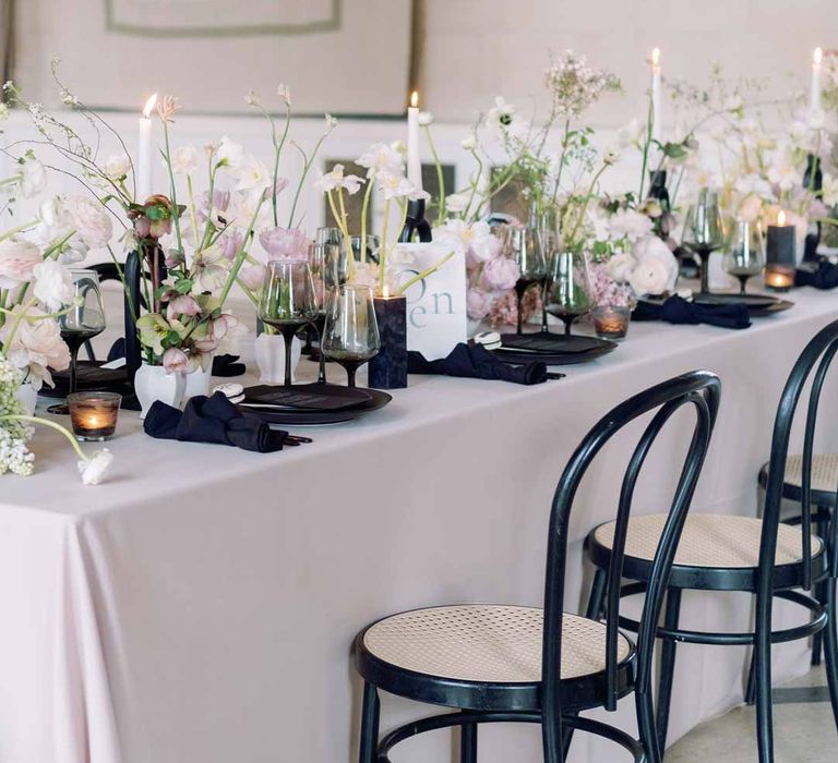 Notan inspired wedding tablescape consisting of light pink wedding tablecloth, white poppies, light pink Persian buttercups, baby's-breath and foliage centrepieces, black artistic candlestick holders, white tapered candles, black crockery and monochrome wedding stationery 