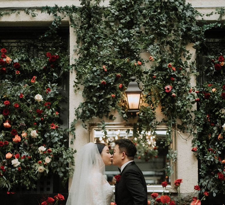 Red, orange, and white roses decorate the wedding venue with the bride in a long sleeve wedding dress and groom in a black tuxedo 