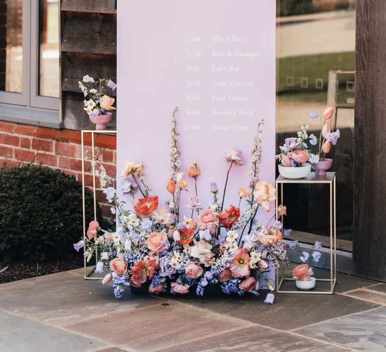 Lilac wedding sign with peach garden roses, white peonies, lilac sweet peas, bluebells and wildflowers floral arrangements 