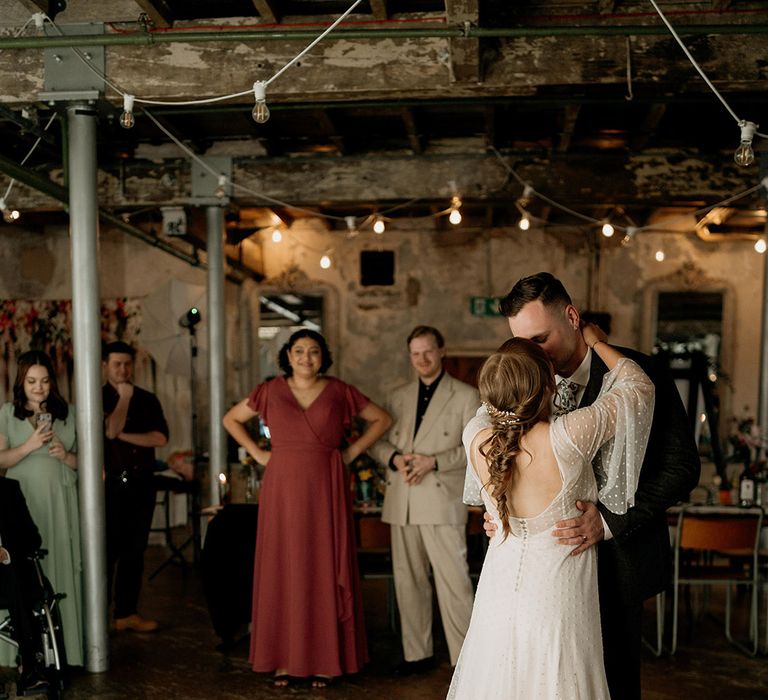 The bride in a dotted wedding dress and groom in grey suit have their first dance together 