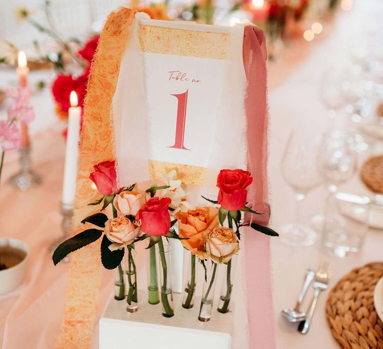 Colourful alternative wedding table number with frayed orange and pink ribbon and test tube vase holders with garden roses 