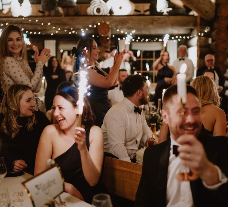 Wedding guests at French destination ski wedding at La Cabane Des Praz holding up indoor wedding sparklers for bride and groom