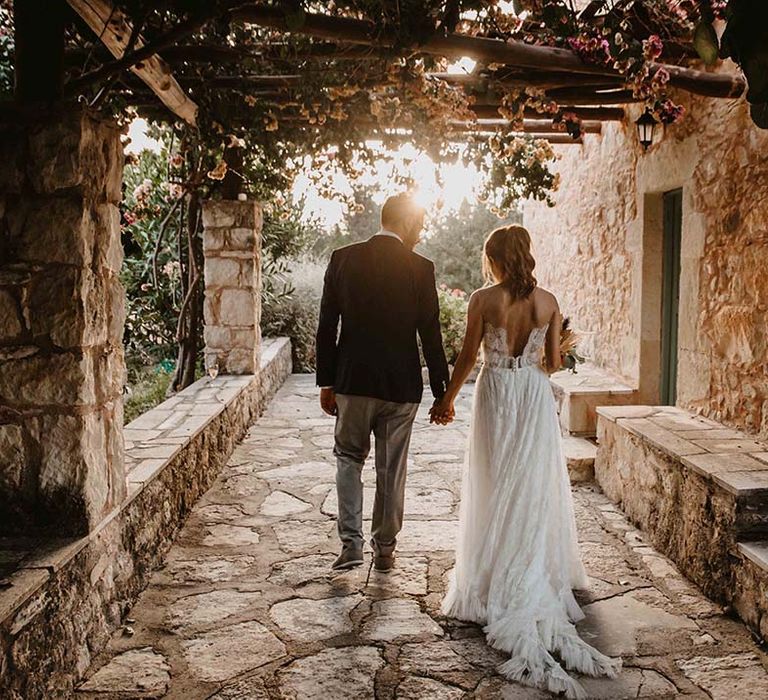 groom in chinos navy and blazer holding hands with his bride in a strapless lace wedding dress at greece destination wedding