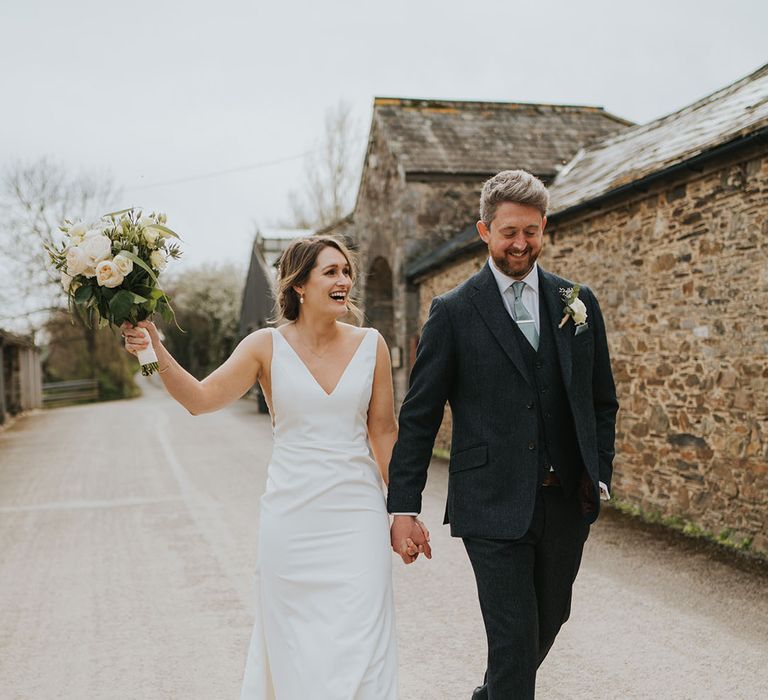 Groom in three piece suit with light green tie with silver tie clip walking hand in hand with the bride in plunging wedding gown 