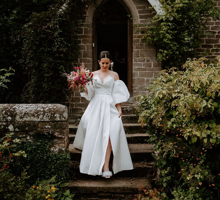 Bride in strapless Suzanne Neville wedding dress with front slit and detachable puff sleeves with pink bouquet 