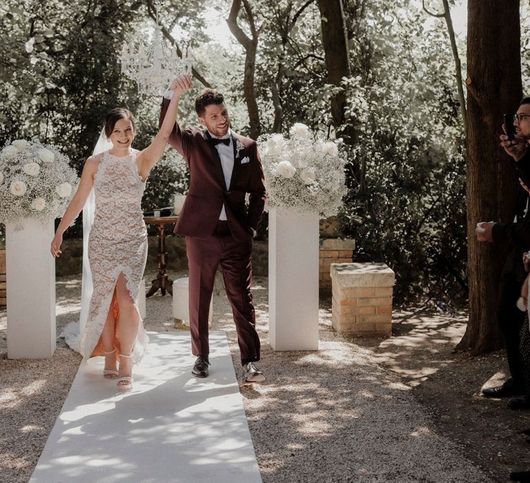 Bride in Grace Loves Lace wedding dress with groom in burgundy suit walking back down the aisle as a married couple 