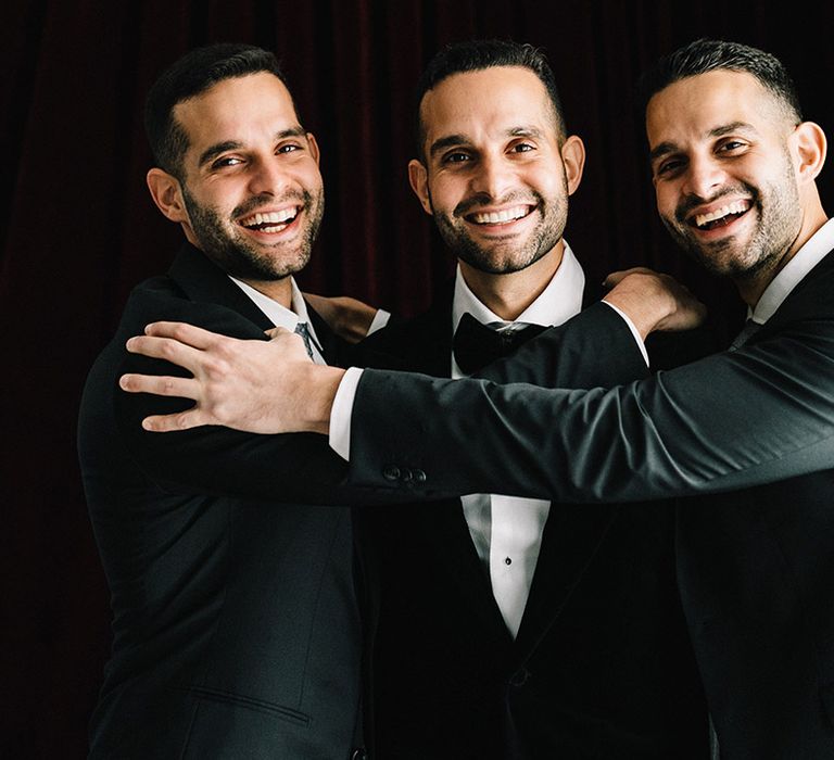 The groom and groomsmen getting ready together for the wedding wearing black tuxedos 