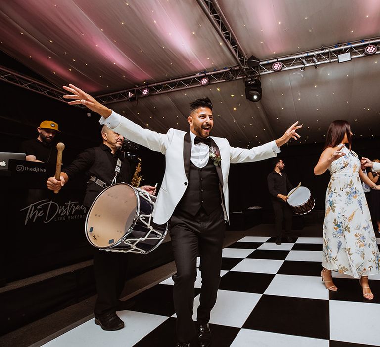 Black and white checkered dance floor with Turkish drummers for traditional wedding entrance by the two grooms 