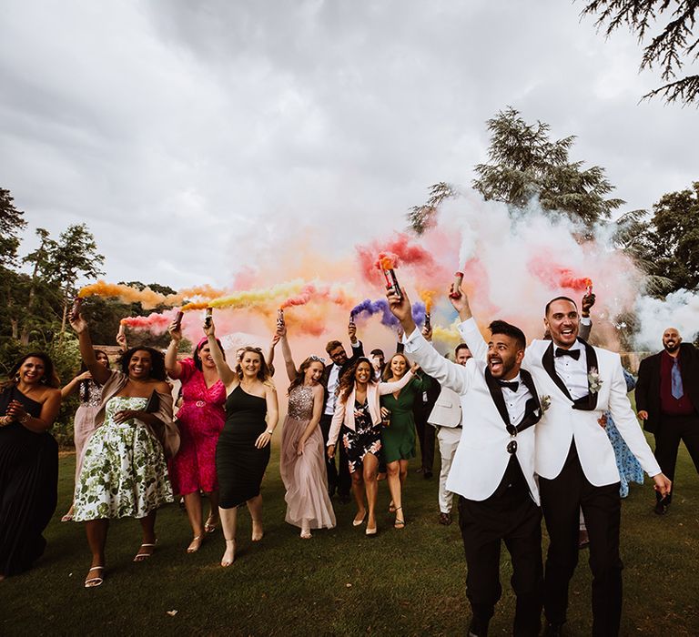 Wedding guests holding up multicoloured wedding smoke bombs for wedding party photo 