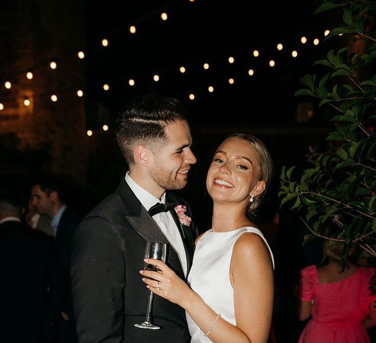 Bride in high neck sleeveless all white short wedding reception dress with groom in black tie at city wedding 