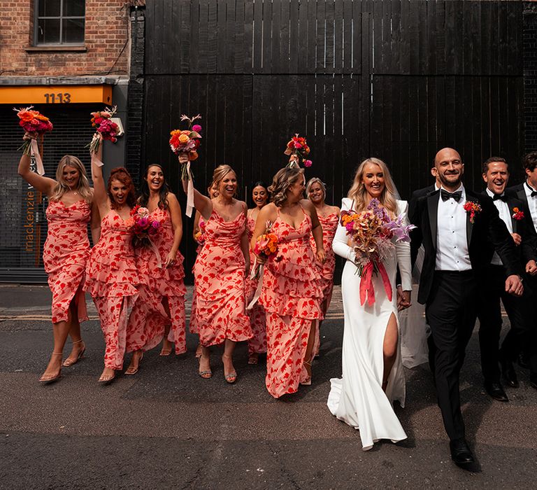 Colourful wedding party with bridesmaids in funky patterned dresses and the groomsmen wear black tuxedos 