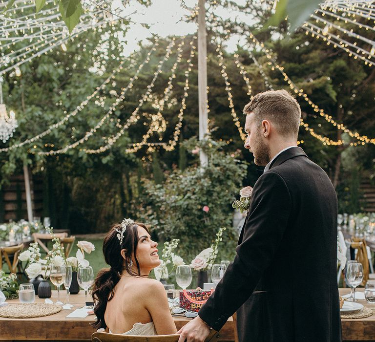 Fairy lights decorate outdoor wedding venue with bride in princess wedding dress and groom in black tux 