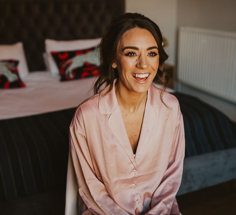 Brown haired bride has makeup done on wedding morning wearing pink satin pyjamas