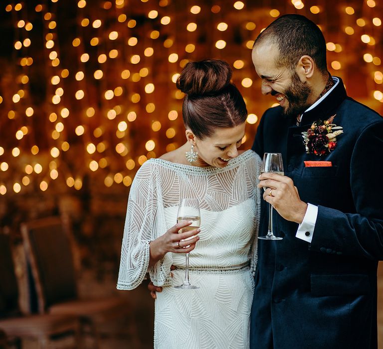 Bride & groom stand in front of twinkling fairy lights