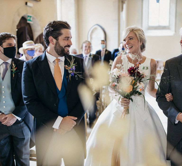 Bride in a Jesus Peiro wedding dress greeting her groom in a morning suit at the end of the church altar 