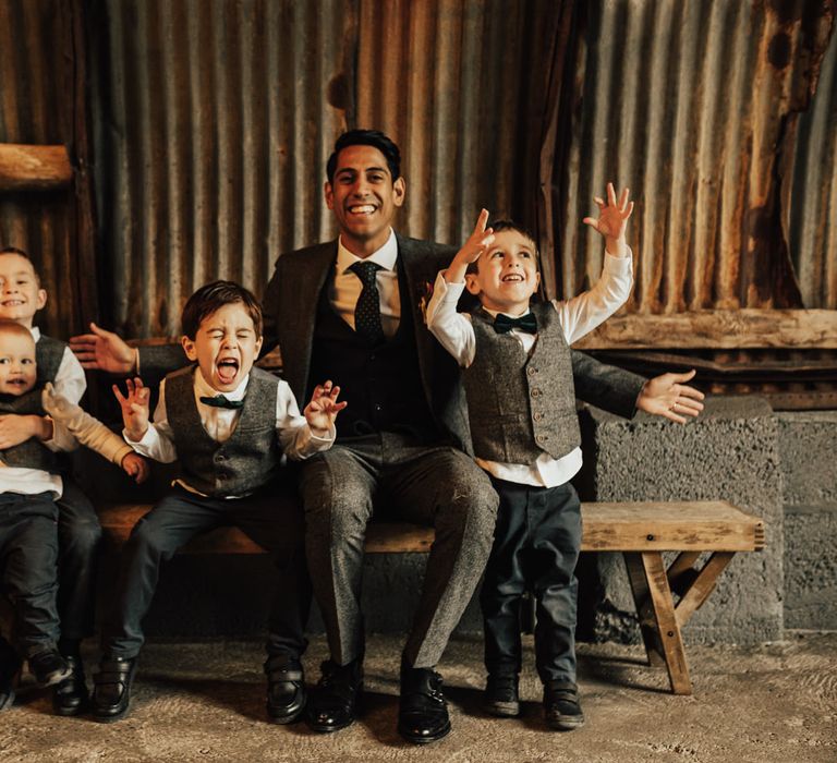 Groom in a grey world suit with navy waistcoat sitting with his little page boys 