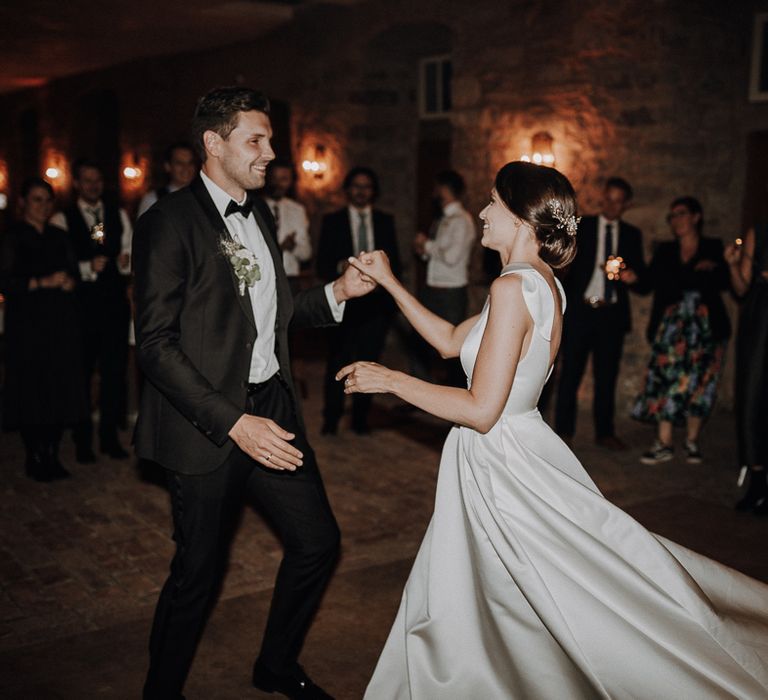 Bride in white Jesus Piero gown dances with groom in black Tiger of Sweden tuxedo at German wedding