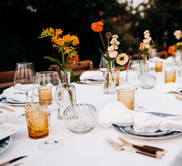 Wedding table decor with yellow goblets, blue tableware and flower stems in bottles 