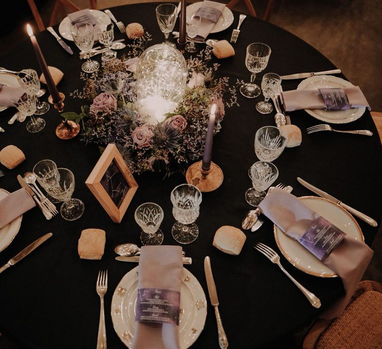 Round wedding table with purple floral centrepiece and a glass bulb filled with fairy lights, with purple starry details