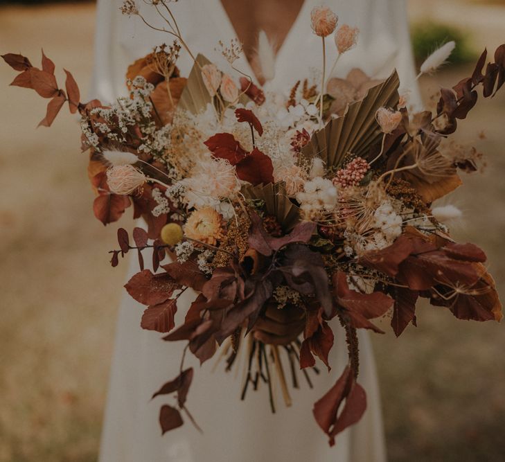 Autumn wedding bouquet with brown foliage, dried palm leaves and orange flowers 