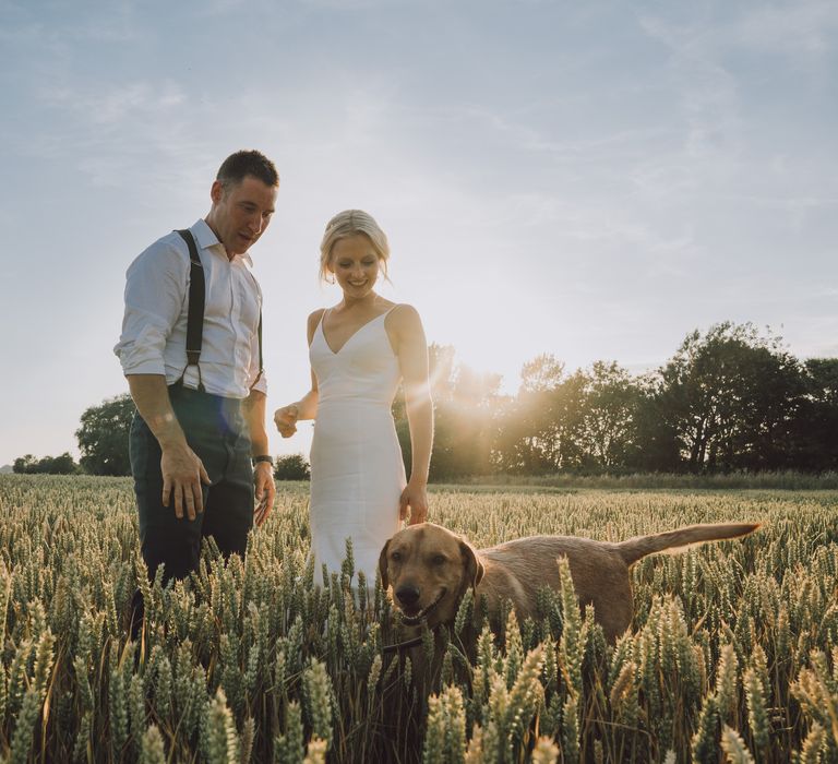 Bride & groom stand in the field with their dog as they have post-wedding photoshoot