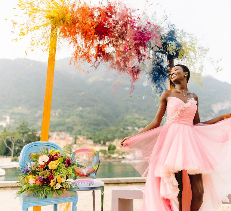 Rainbow coloured pampas grass archway stands behind bride in pastel pink wedding gown