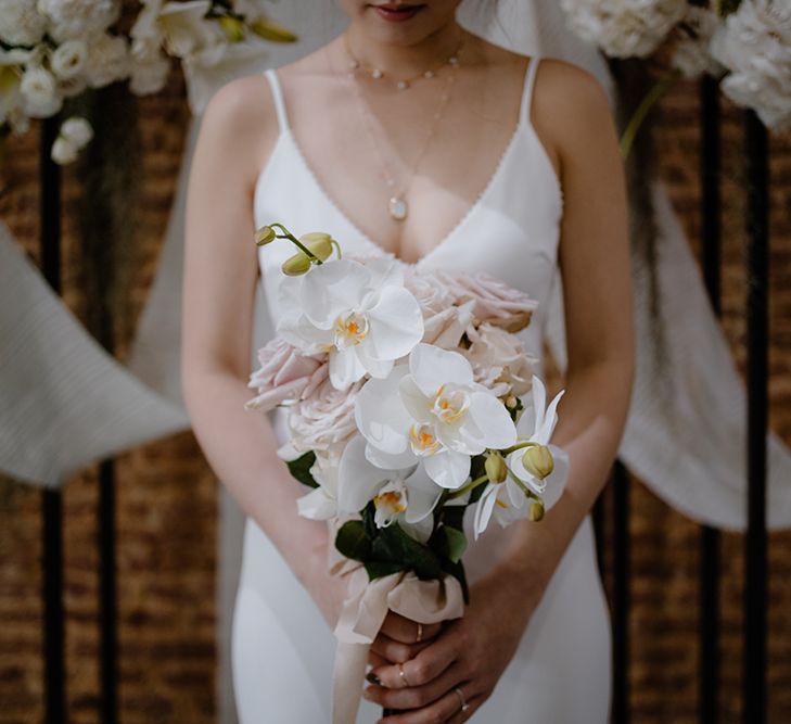 Bride in a minimalist wedding dress holding a white orchid wedding bouquet 