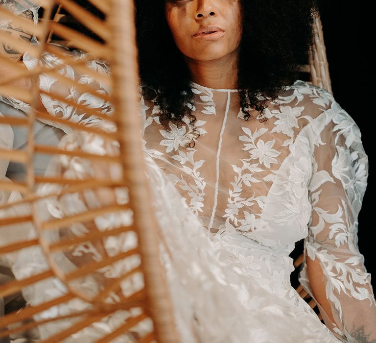 Bride sits on wicker chair and looks toward camera with afro hair styled naturally