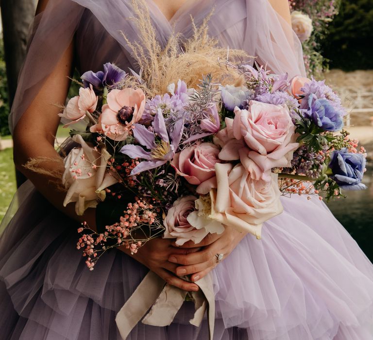 Bride wears purple chiffon gown whilst holding bright and bold bouquet 