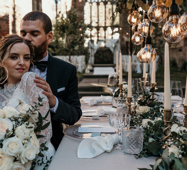 Bride and groom sitting at their elegant green, gold and glass wedding reception table in black-tie attire 