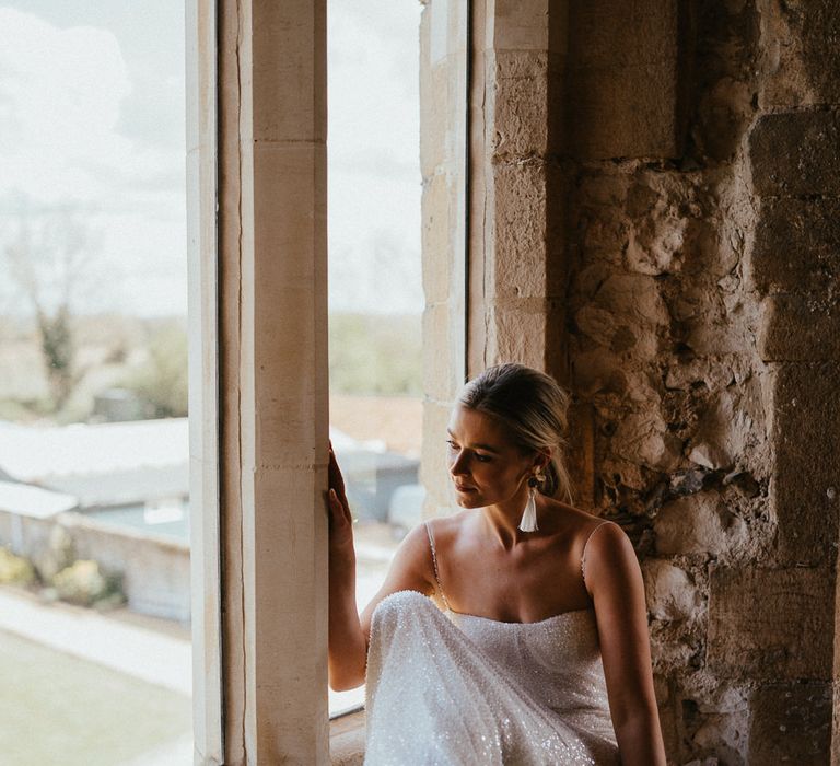 Bride in a white embellished wedding dress with thin straps and tassel earrings