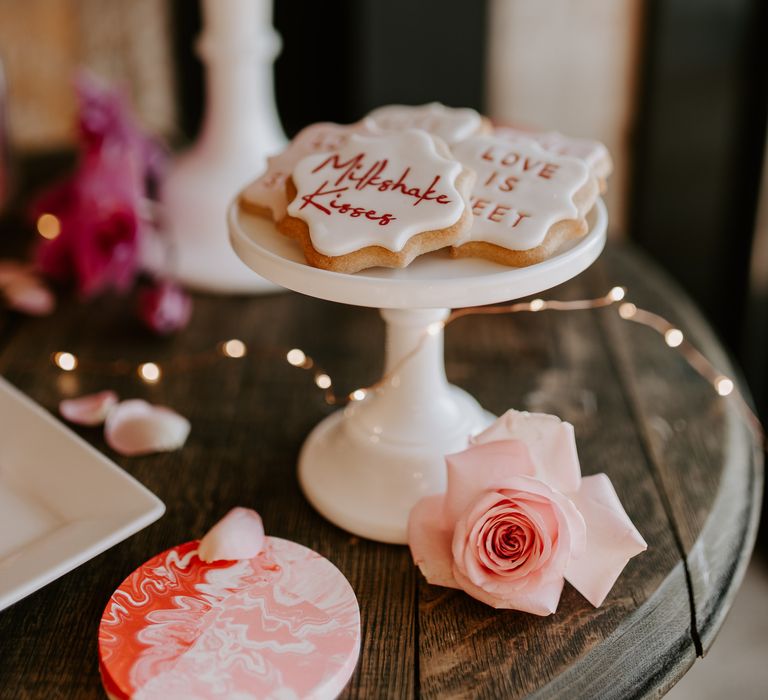 Individual iced biscuits on a white cake stand at wedding dessert table 