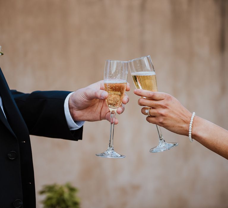 Bride & groom cheers champagne glasses and bride wears pearl bracelet on her wrist