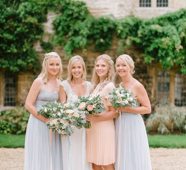 Bride in white dress holding bouquet in portrait with three bridesmaids in pastel blue and peach dresses