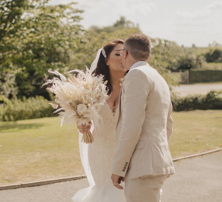 Groom in a beige linen suit kissing his bride in a fitted lace wedding dress with fishtail skirt 