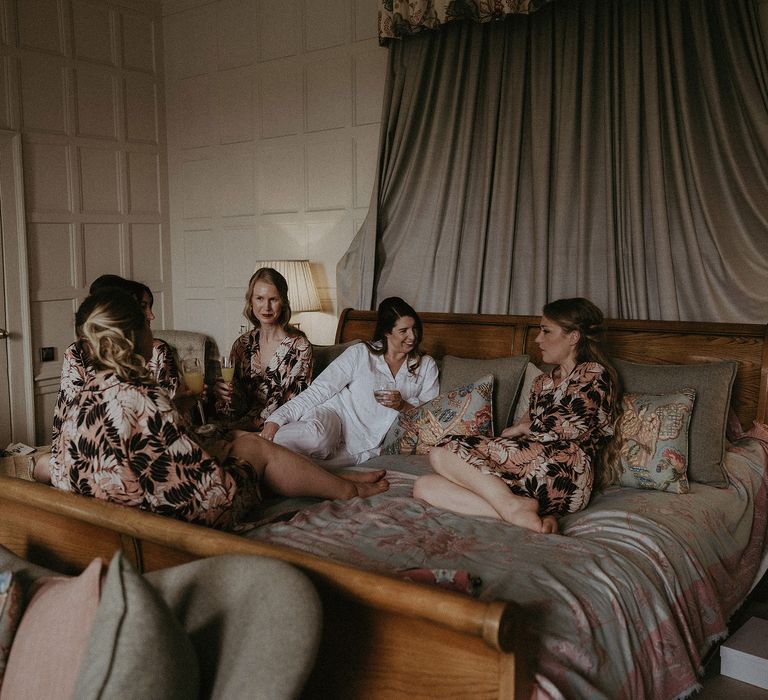 Bride sits with her bridesmaids on the morning of her wedding as bridesmaids wear floral dressing gowns and drink champagne