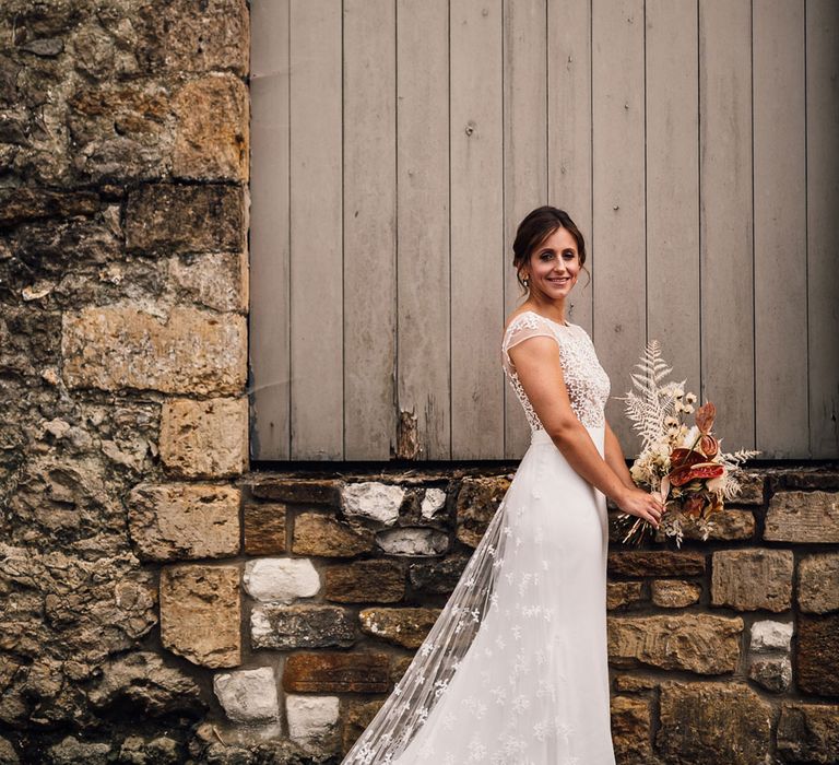 Bride in white open back Rime Arodaky wedding dress with lace train holding dried bridal bouquet for summer wedding in Dorset