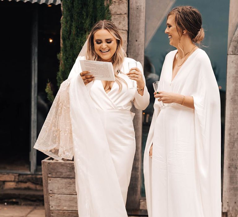 Brides stand with one another outdoors in their white bridal jumpsuits