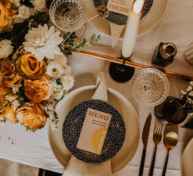 Contemporary place setting with beige charger plate, black polka dot tableware and contemporary on the day wedding stationery 