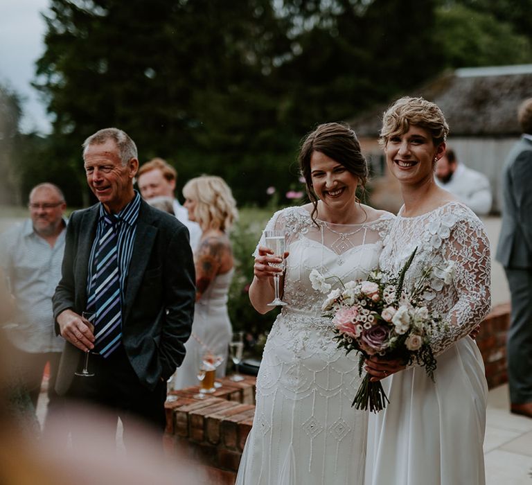 Two brides in a long sleeve wedding dress and vintage inspired gown at their outdoor drinks reception at Woolas Barn 