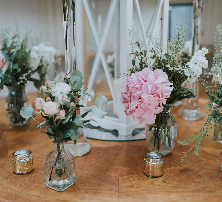 Pink and white florals with green foliage in glass bottles with small silver candle holders on round wooden table for summer wedding at Primrose Hill Farm