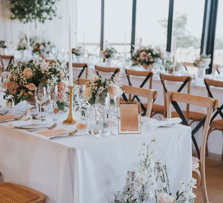 Long white wedding tables with wooden chairs, mixed florals, white dinner candles and glassware for summer wedding at Primrose Hill Farm