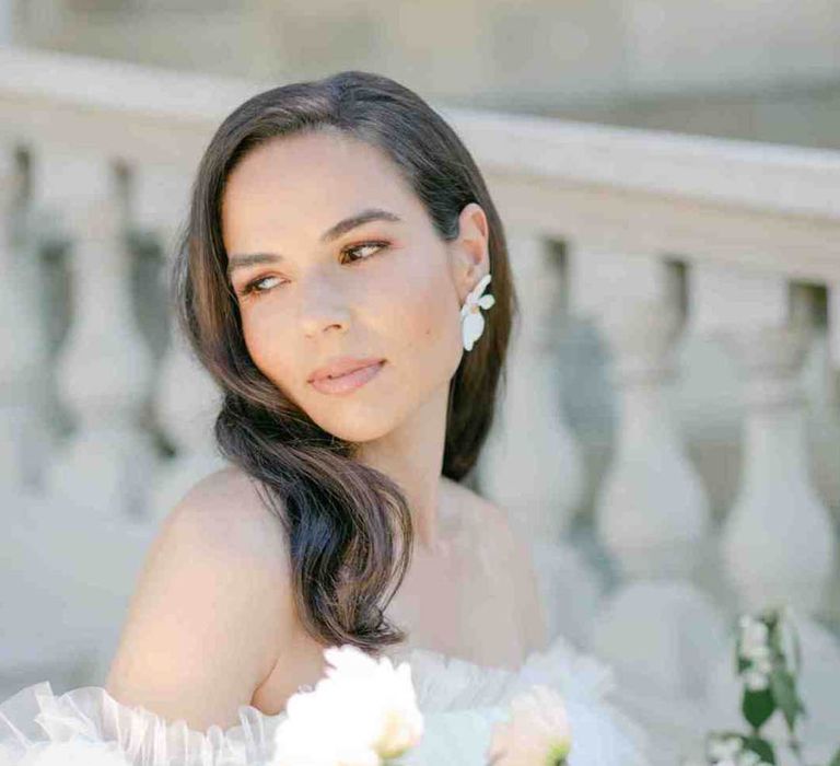 Beautiful bride with long brown hair in an off the shoulder wedding dress holding a pastel flower wedding bouquet 