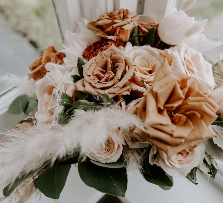 Dusky orange, and blush pink roses with green foliage and dried grass bridal bouquet for DIY garden wedding