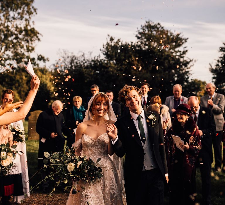 Guests throw wedding confetti over bride and groom