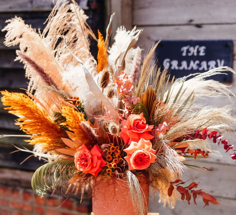 Orange, white and green rose and pampas grass florals in orange vase for festival style wedding