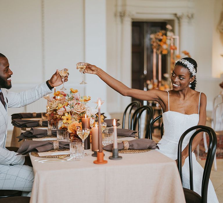 Black bride and groom toasting champagne over orange and neutral wedding table decor at Kirtlington Park wedding venue in Oxfordshire 