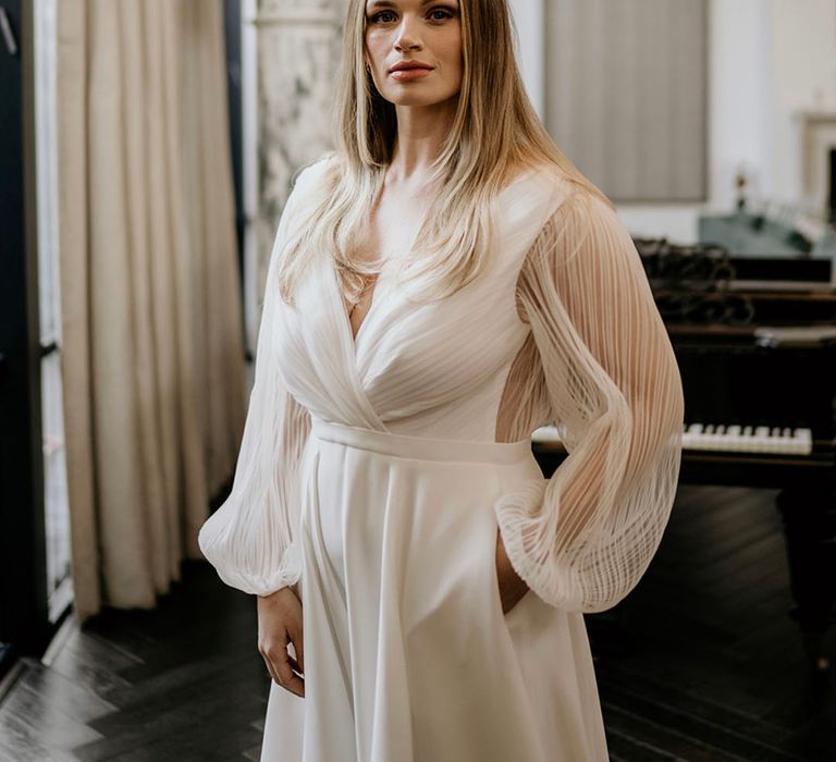 Bride with long blonde hair wearing a sheer pleated long sleeve wedding dress