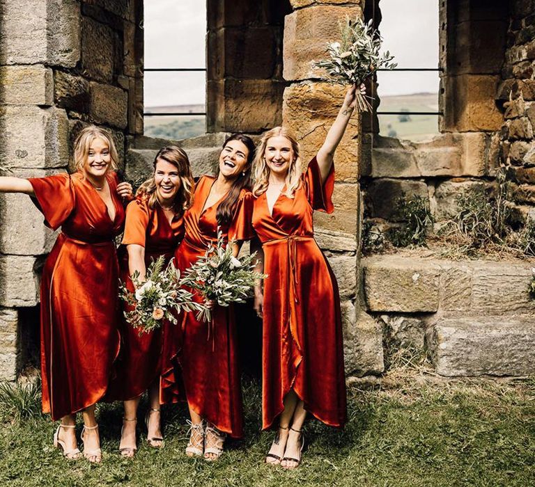 Bridesmaids in burnt orange satin wrap bridesmaid dresses holding bouquets 